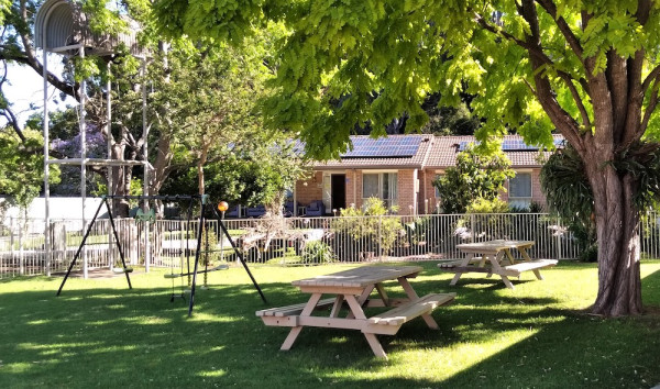 Hope House Batemans Bay backyard including trees, a swing set and picnic tables.