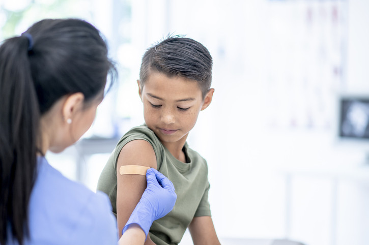 Female nurse placing band aid over young boys' vaccination.