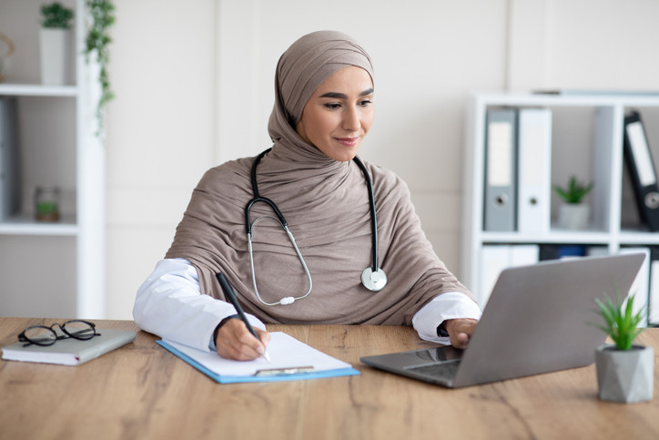 Doctor on laptop, taking notes.