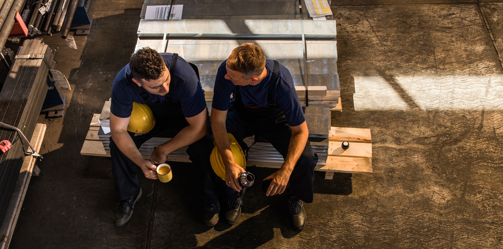 Two men sitting on the back of a ute speaking whilst having a coffee