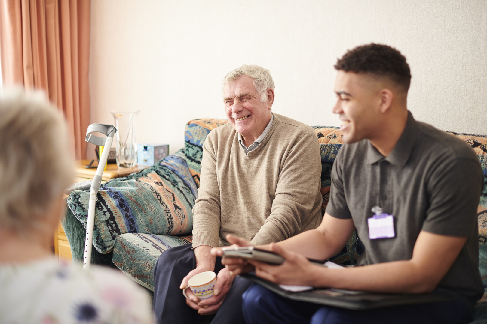 Health professional sitting on a couch with an elderly man talking.