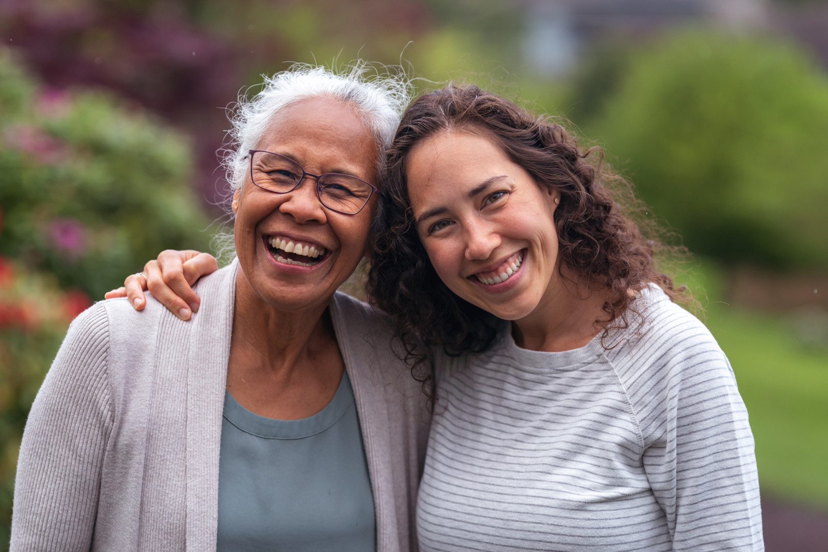 Young woman hugging an elderly woman surrounded by parkland.