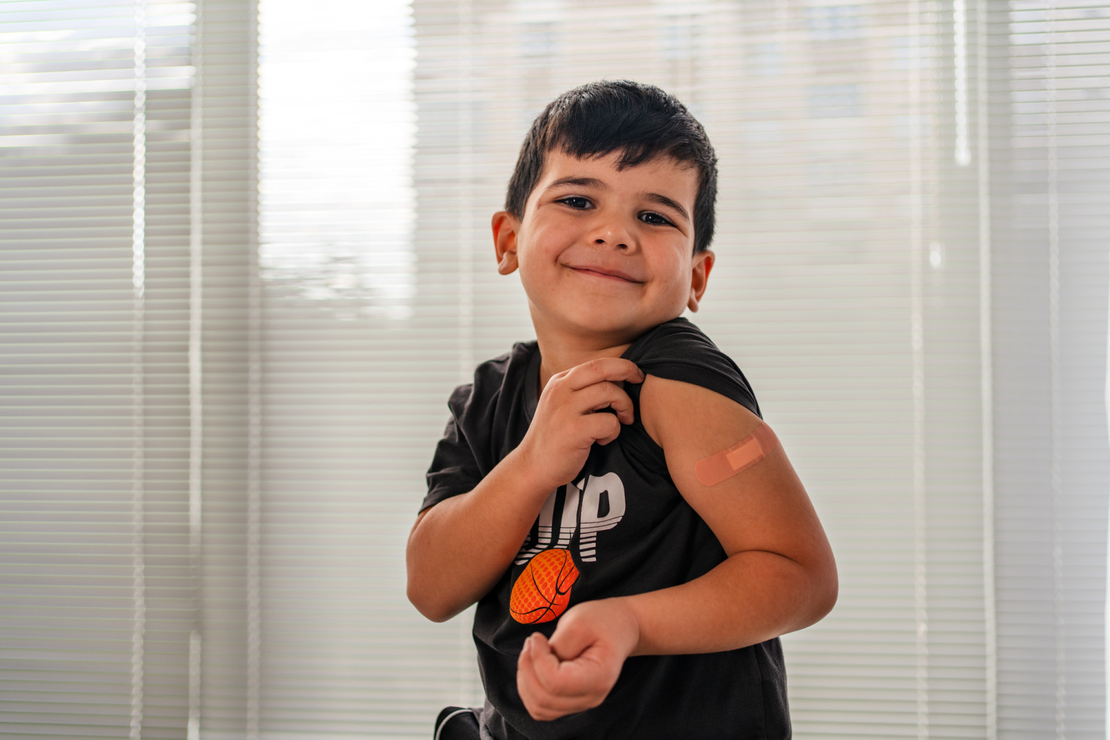 Young boy showing bandaid on arm after immunisation.