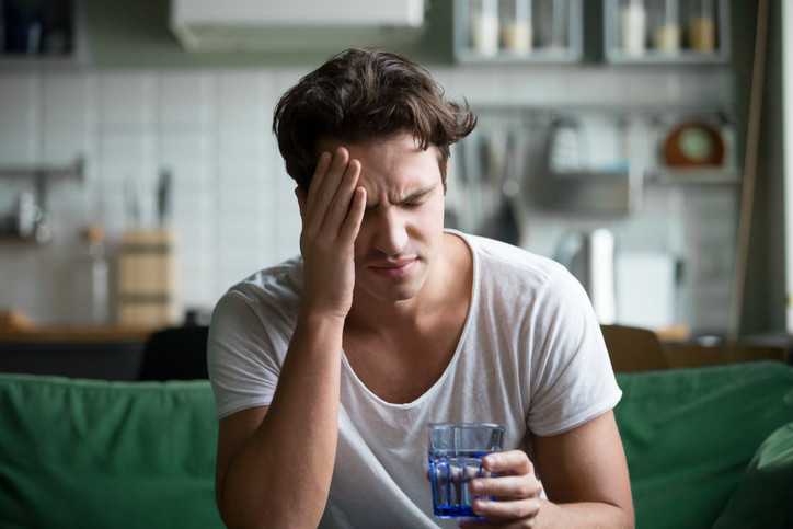 Young man, hungover with hand on head.