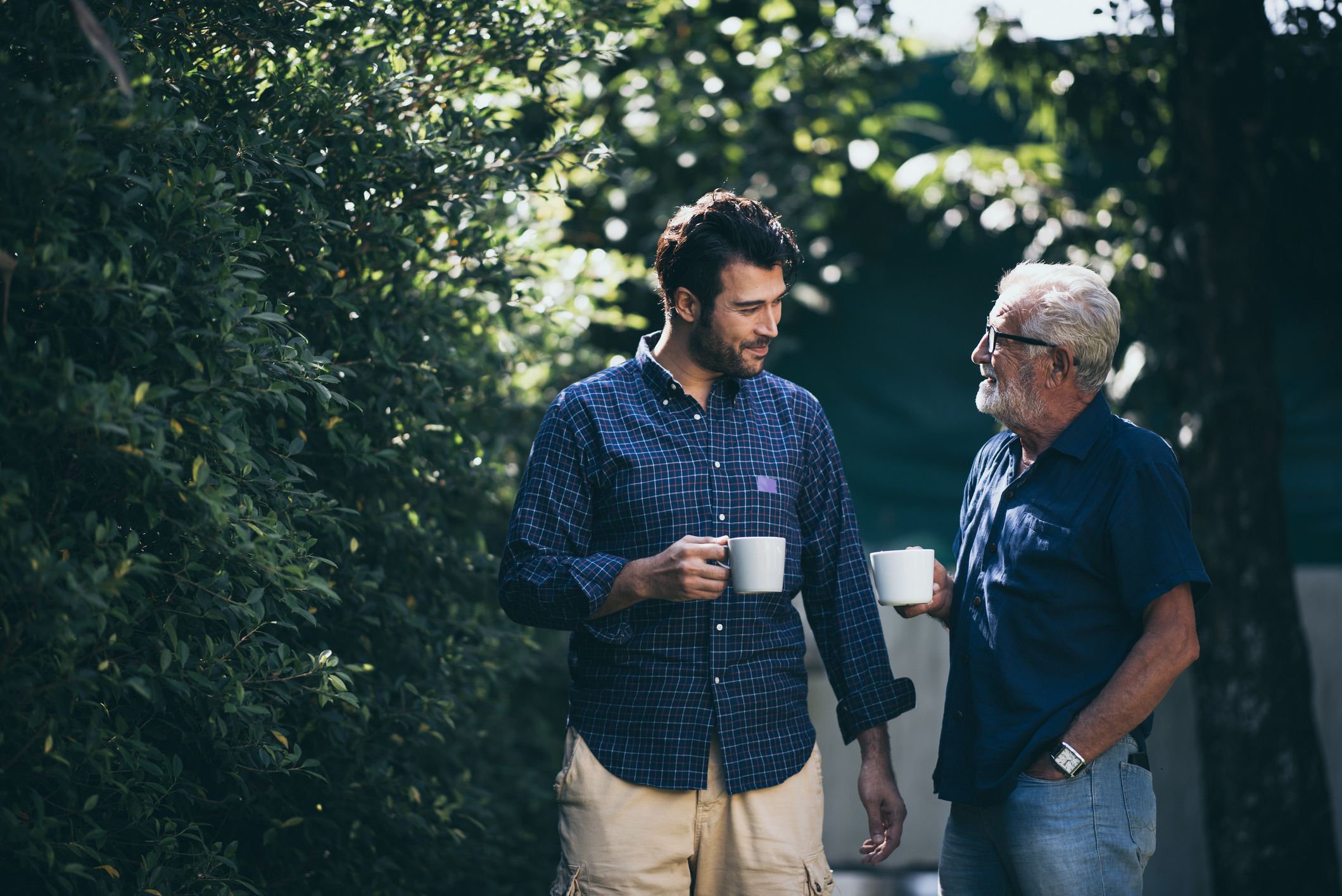 Older man and a younger man sitting outside talking a having a cup of tea together