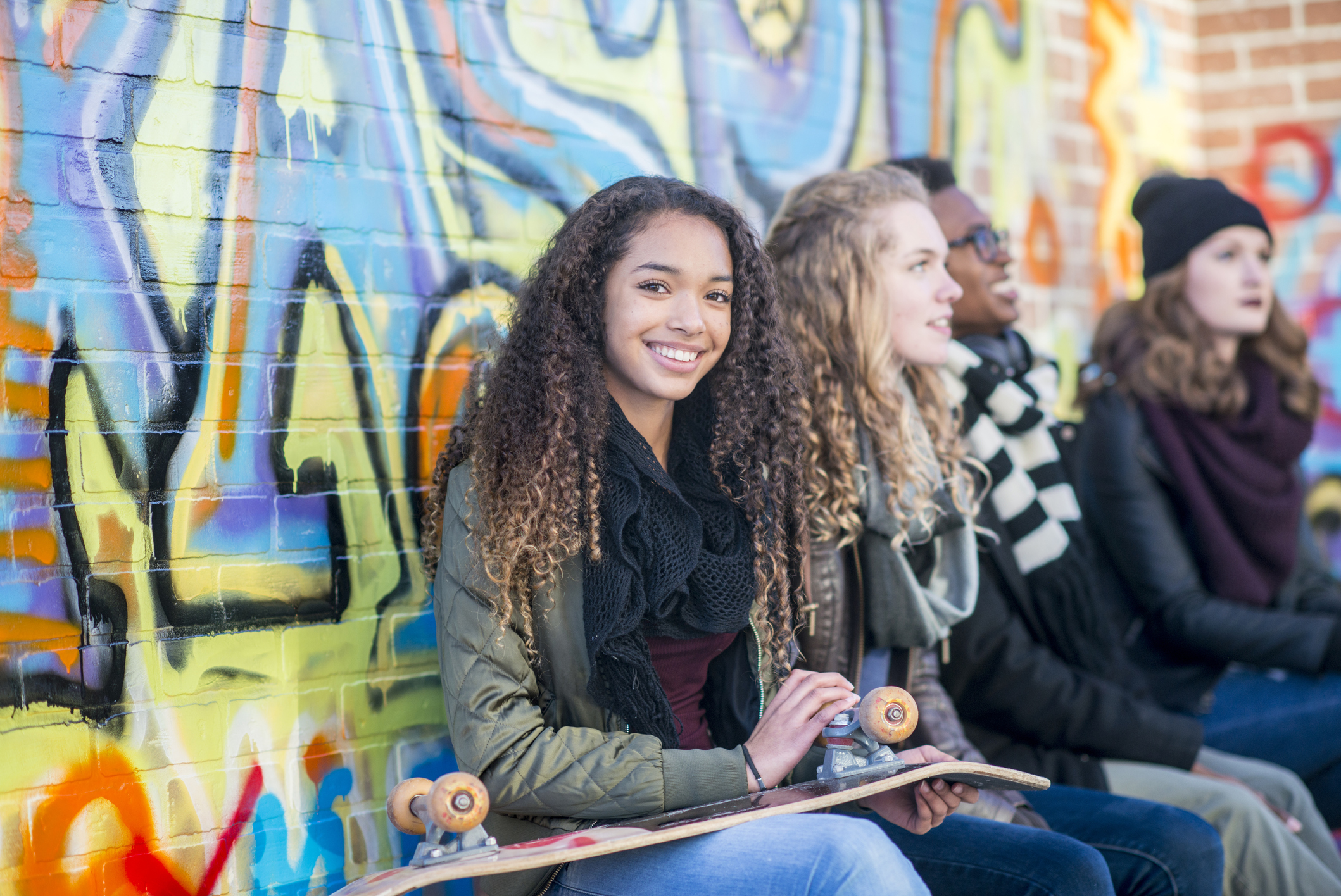 Children talking and smiling in front of a vibrant colourful graffiti wall.