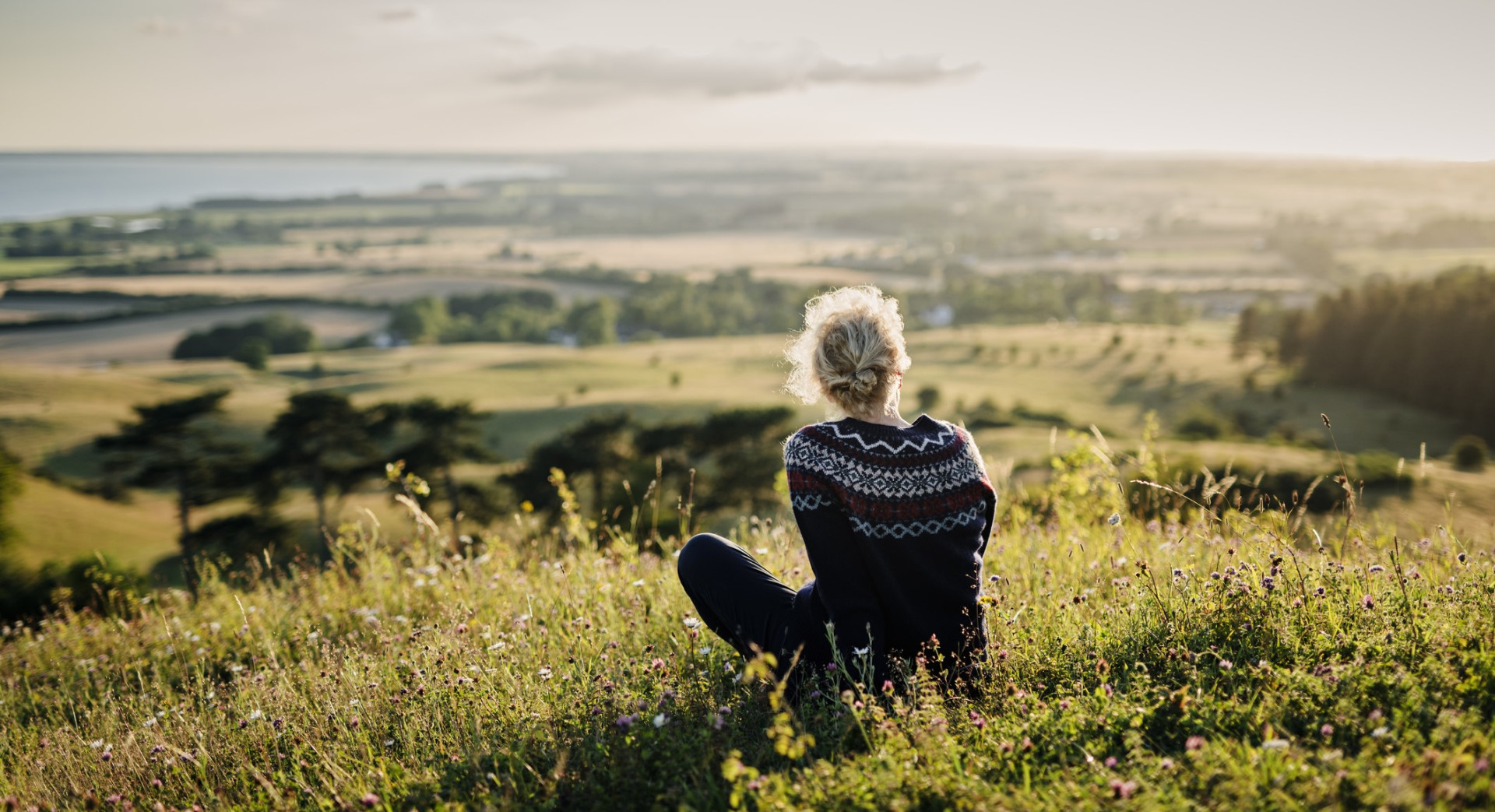 A young lady sitting on a hill in the country side